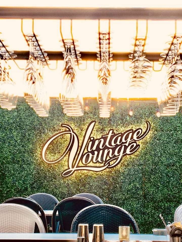 Vintage Lounge custom neon sign on green hedge wall